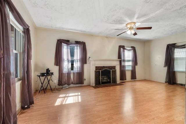 unfurnished living room featuring a ceiling fan, a textured ceiling, wood finished floors, and a fireplace