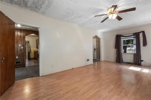 spare room featuring arched walkways, light wood finished floors, a textured ceiling, and ceiling fan