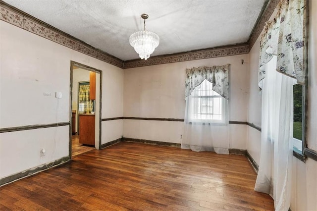 empty room featuring an inviting chandelier, wood finished floors, and a textured ceiling