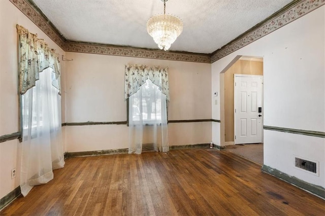 empty room featuring arched walkways, visible vents, a textured ceiling, and hardwood / wood-style floors