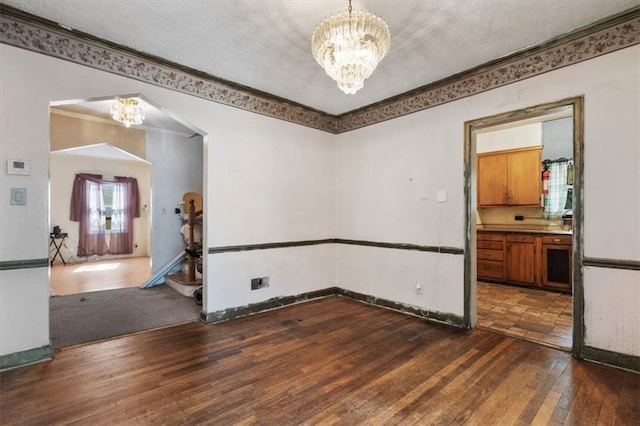 spare room featuring a notable chandelier, dark wood finished floors, crown molding, and a textured ceiling