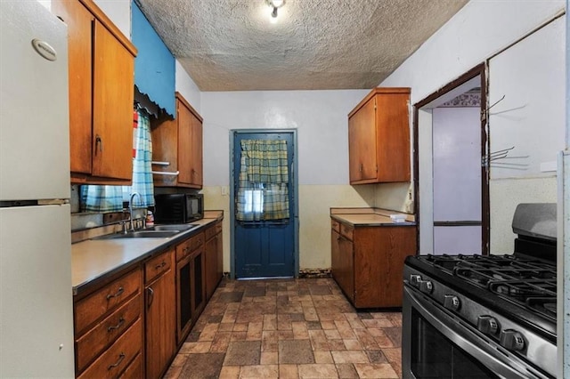 kitchen with stainless steel gas range, brown cabinets, freestanding refrigerator, and a sink