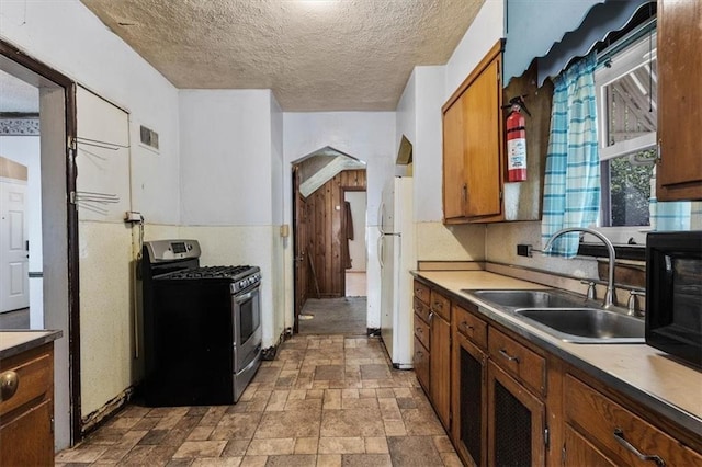 kitchen with stainless steel range with gas cooktop, freestanding refrigerator, arched walkways, stone finish floor, and a sink