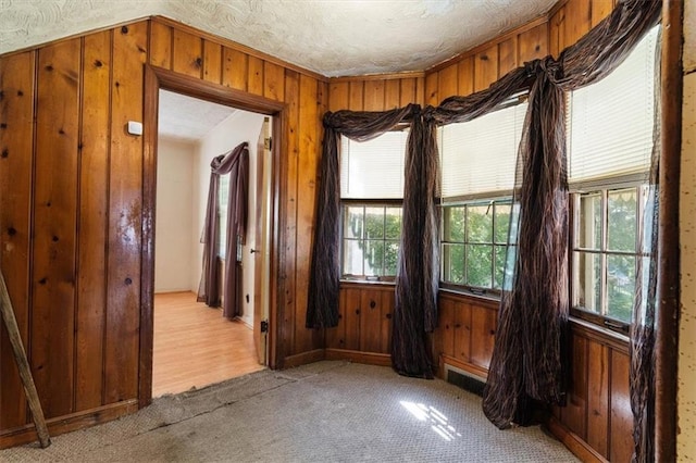 empty room featuring wooden walls, light colored carpet, visible vents, and a textured ceiling