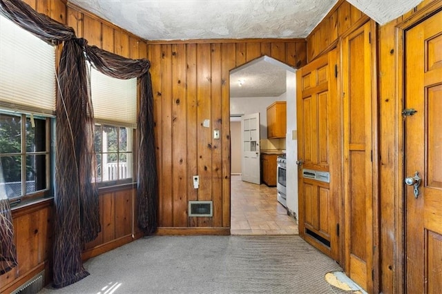 empty room with visible vents, light colored carpet, wood walls, and a textured ceiling