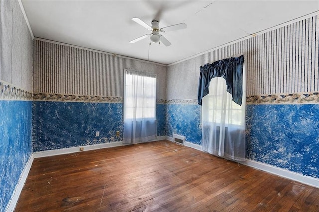 empty room featuring visible vents, a ceiling fan, wood-type flooring, wallpapered walls, and baseboards