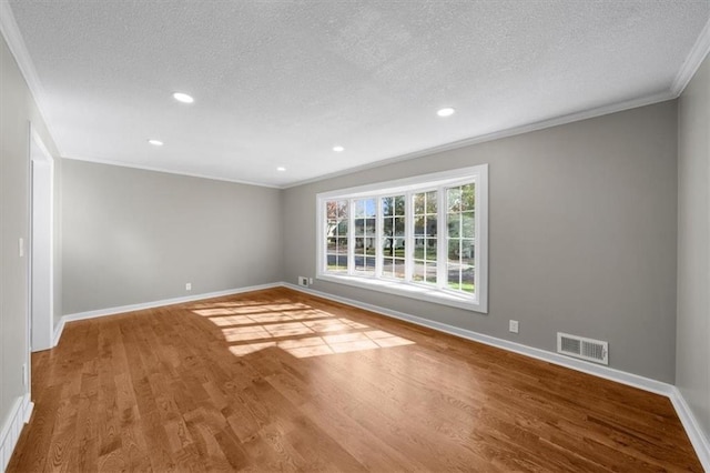 unfurnished room featuring wood finished floors, baseboards, visible vents, ornamental molding, and a textured ceiling