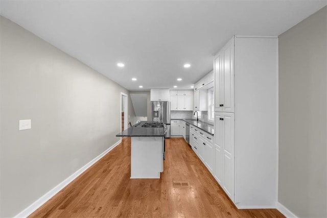 kitchen with a sink, stainless steel appliances, light wood-style floors, white cabinetry, and dark countertops