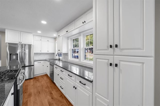 kitchen featuring dark stone countertops, backsplash, wood finished floors, stainless steel appliances, and white cabinets