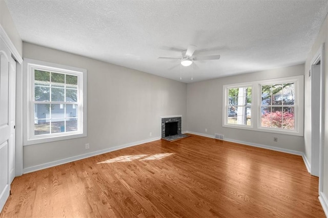 unfurnished living room featuring visible vents, light wood-style flooring, a ceiling fan, a fireplace, and baseboards