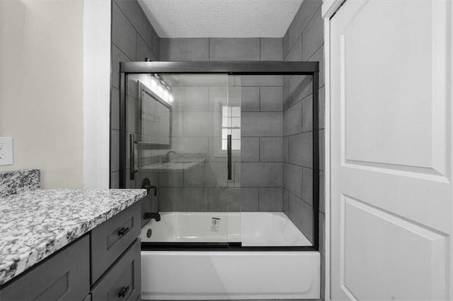 full bath with vanity, shower / bath combination with glass door, and a textured ceiling