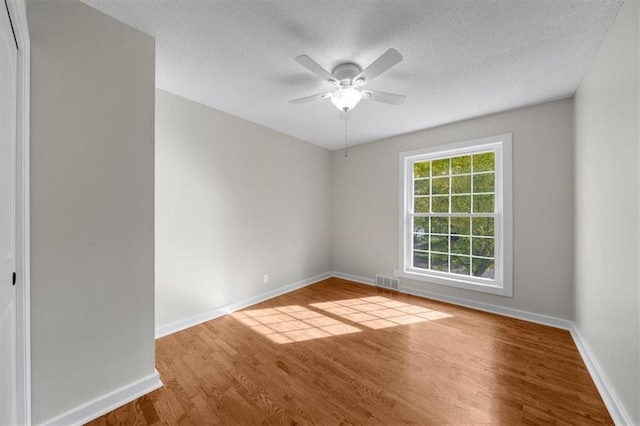 empty room with visible vents, a ceiling fan, a textured ceiling, wood finished floors, and baseboards