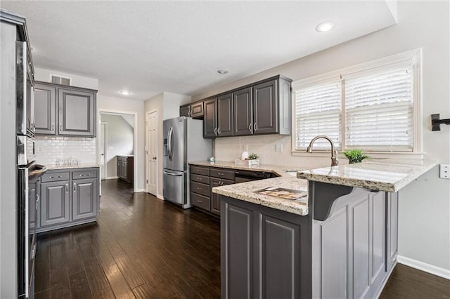 12109 Overbrook Ct, Leawood, KS 66209 - kitchen featuring appliances with stainless steel finishes, a peninsula, light stone counters, dark wood-style flooring, and decorative backsplash