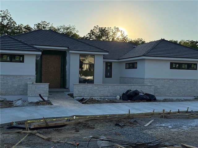 7410 NW Pampas Ln, Parkville, MO 64152 - back of house at dusk with stone siding, stucco siding, and a tile roof