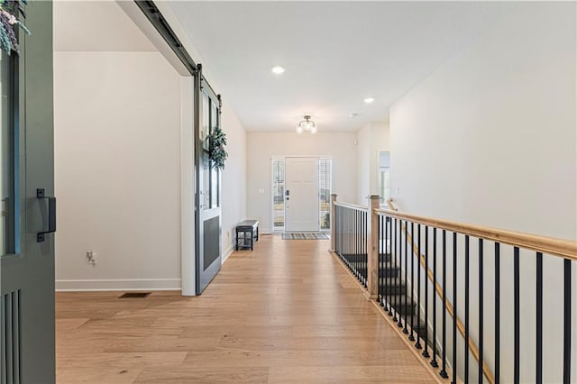 hallway featuring light wood finished floors, recessed lighting, baseboards, and a barn door