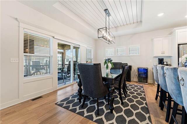 dining room with baseboards, visible vents, light wood finished floors, a raised ceiling, and wooden ceiling