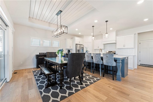 dining space with a tray ceiling, recessed lighting, baseboards, and light wood finished floors