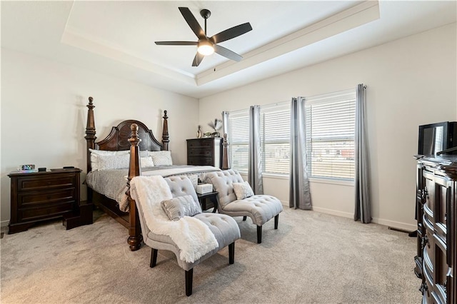 bedroom featuring light colored carpet, baseboards, a tray ceiling, and a ceiling fan