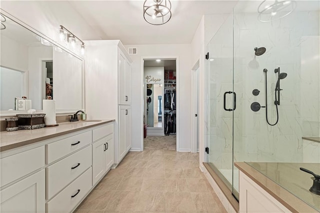 full bathroom with vanity, visible vents, a marble finish shower, baseboards, and a walk in closet