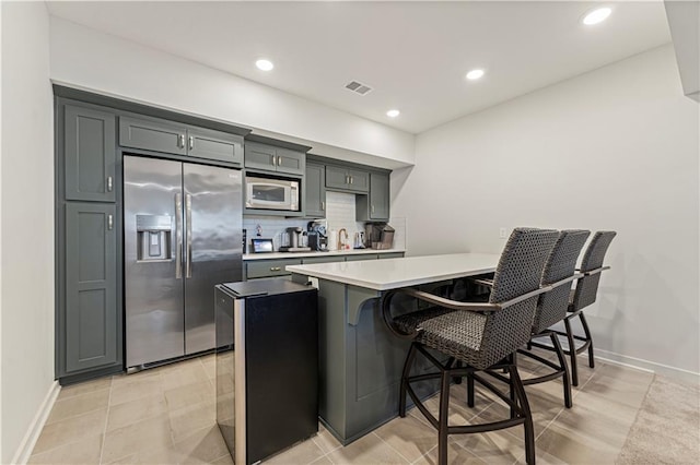 kitchen with white microwave, visible vents, a breakfast bar area, a peninsula, and stainless steel fridge