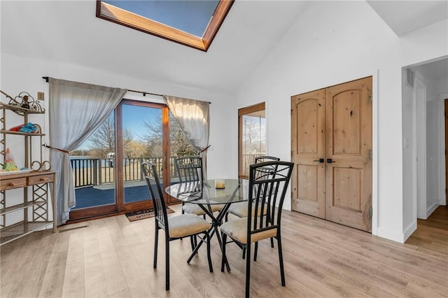 dining area featuring a skylight, baseboards, high vaulted ceiling, and light wood-style flooring