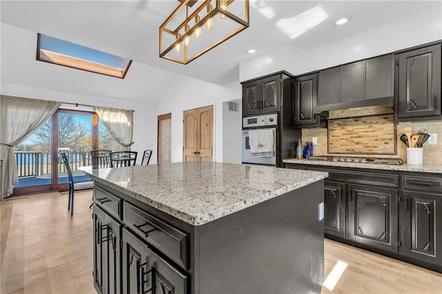 kitchen with lofted ceiling with skylight, backsplash, a kitchen island, dark cabinetry, and appliances with stainless steel finishes