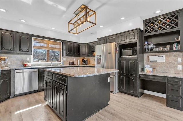 kitchen with a center island, light stone countertops, light wood-type flooring, appliances with stainless steel finishes, and a sink