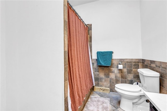 full bath featuring tile patterned floors, a wainscoted wall, toilet, tile walls, and vanity