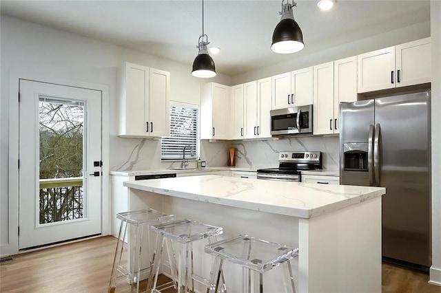 kitchen with a sink, a kitchen island, white cabinetry, appliances with stainless steel finishes, and light stone countertops