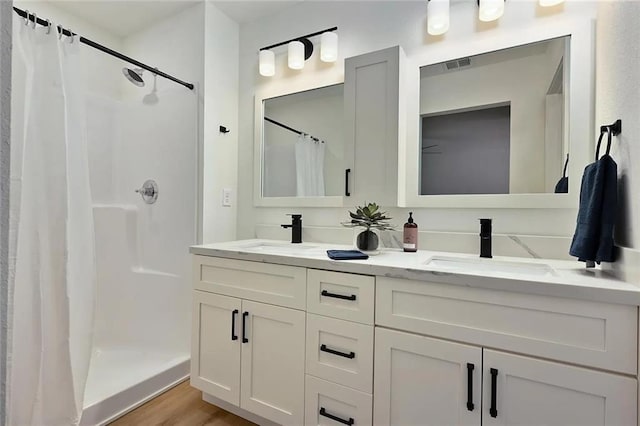 bathroom featuring double vanity, visible vents, a shower stall, and a sink