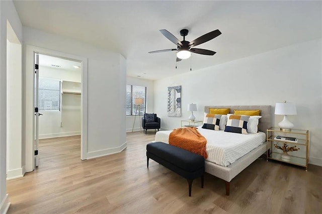 bedroom with light wood-style flooring, a spacious closet, baseboards, and ceiling fan