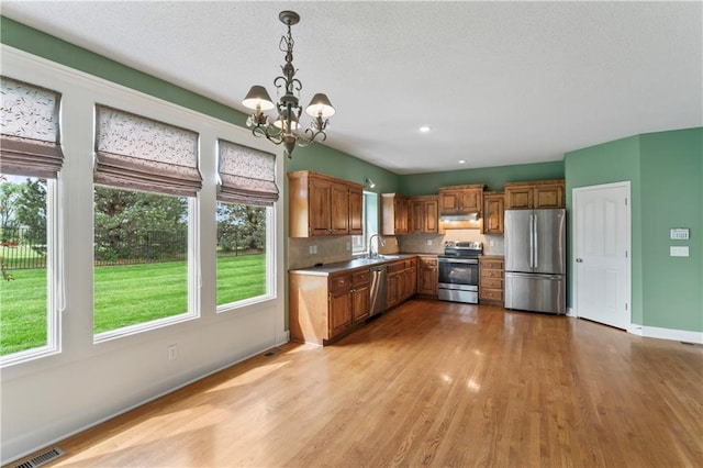 24987 W 150th Ct, Olathe, KS 66061 - kitchen featuring brown cabinetry, stainless steel appliances, under cabinet range hood, an inviting chandelier, and light wood-style floors