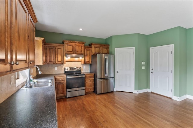 24987 W 150th Ct, Olathe, KS 66061 - kitchen featuring under cabinet range hood, brown cabinetry, a sink, decorative backsplash, and stainless steel appliances