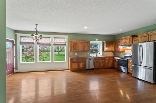 24987 W 150th Ct, Olathe, KS 66061 - kitchen featuring stainless steel appliances, brown cabinets, a textured ceiling, dark wood-style flooring, and a notable chandelier