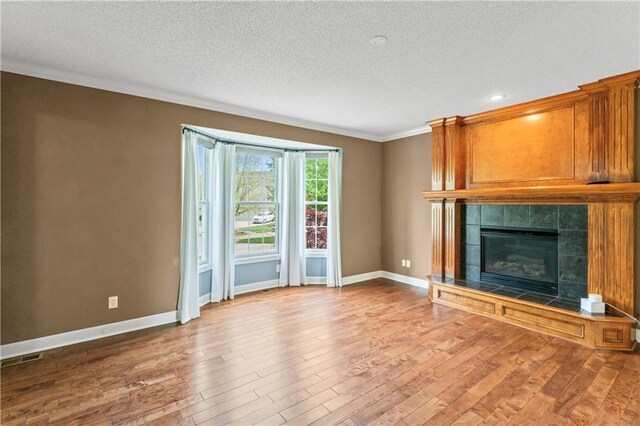 24987 W 150th Ct, Olathe, KS 66061 - unfurnished living room featuring ornamental molding, a textured ceiling, wood finished floors, a tiled fireplace, and baseboards