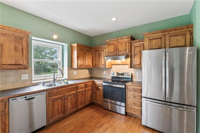 24987 W 150th Ct, Olathe, KS 66061 - kitchen with appliances with stainless steel finishes, a sink, under cabinet range hood, brown cabinetry, and wood finished floors