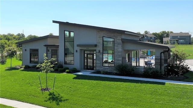 modern home featuring stone siding, stucco siding, a front yard, and fence