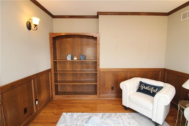 living area featuring a wainscoted wall, wood finished floors, and crown molding