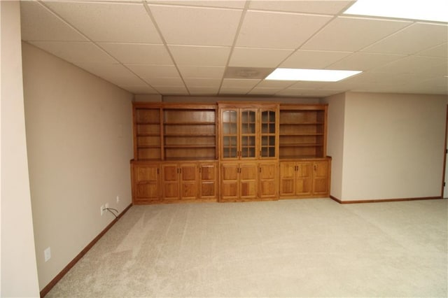 empty room with a drop ceiling, light colored carpet, and baseboards