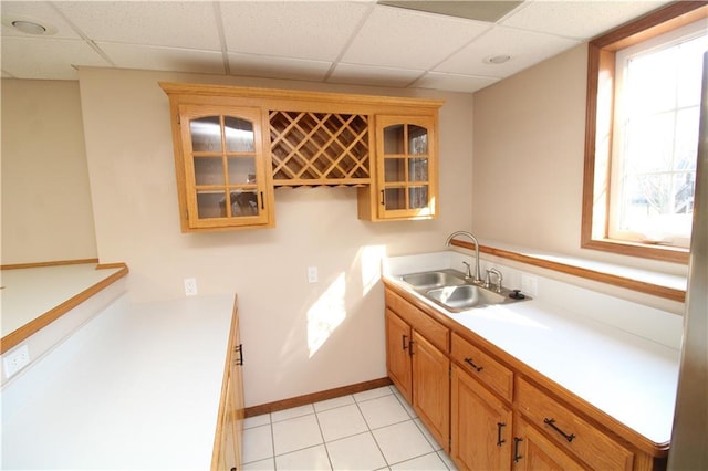 kitchen with glass insert cabinets, baseboards, a drop ceiling, light countertops, and a sink