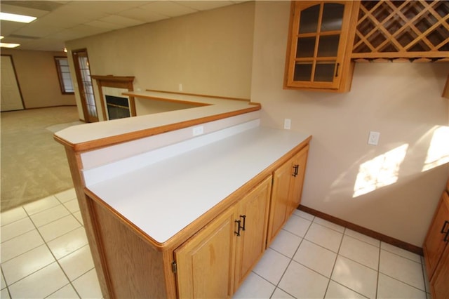 kitchen featuring glass insert cabinets, light countertops, light tile patterned floors, a peninsula, and a paneled ceiling