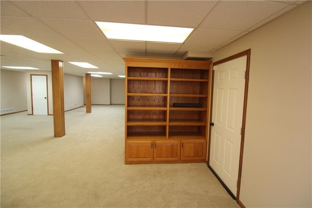 finished below grade area with visible vents, light colored carpet, a paneled ceiling, and baseboards