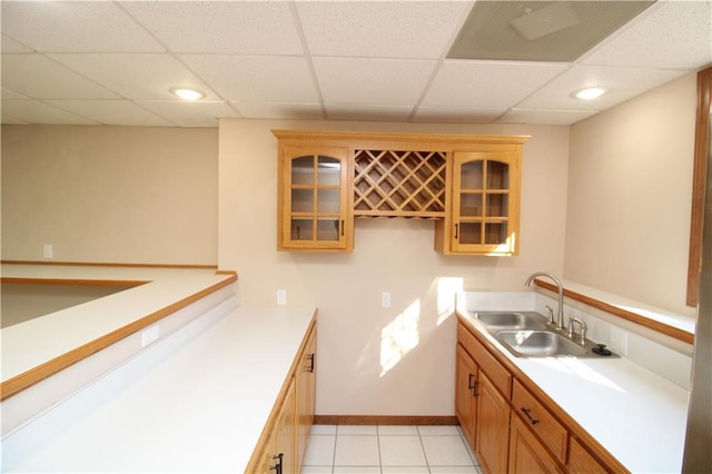 kitchen with glass insert cabinets, baseboards, light countertops, light tile patterned floors, and a sink