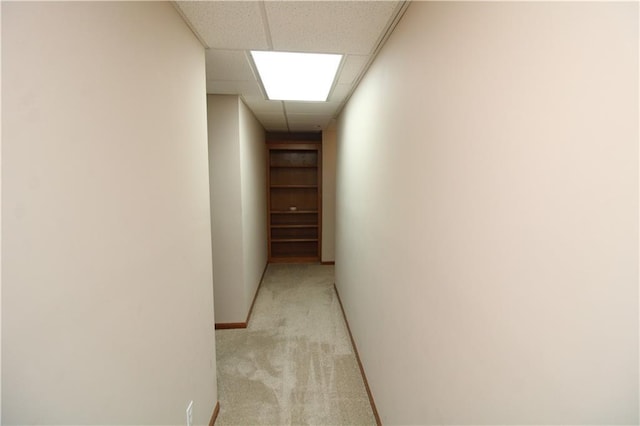 corridor featuring light colored carpet, baseboards, and a paneled ceiling