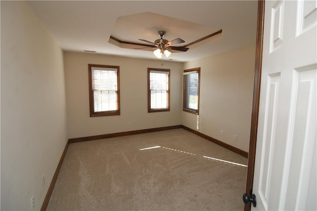 carpeted spare room with a raised ceiling, a ceiling fan, baseboards, and visible vents