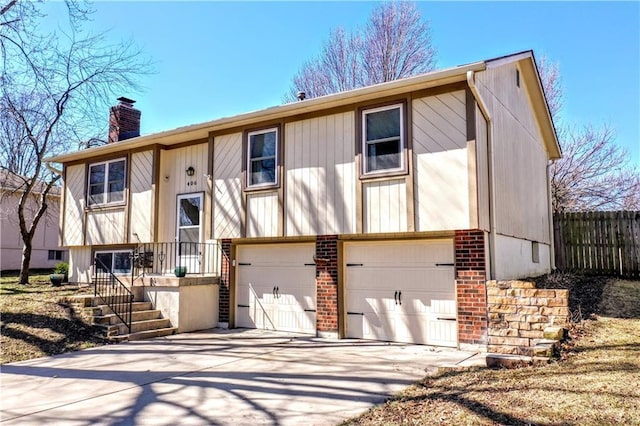 bi-level home featuring driveway, fence, an attached garage, brick siding, and a chimney