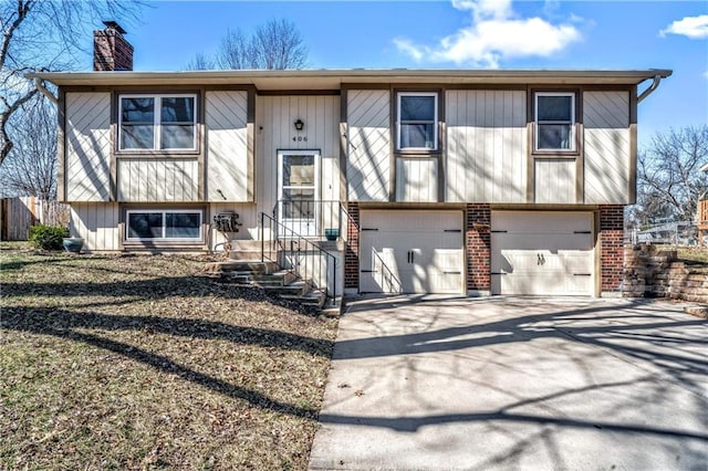 split foyer home featuring concrete driveway, a garage, brick siding, and a chimney