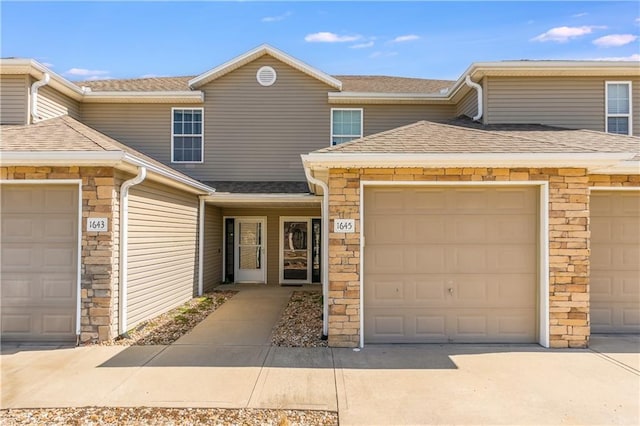 multi unit property with an attached garage, concrete driveway, and roof with shingles