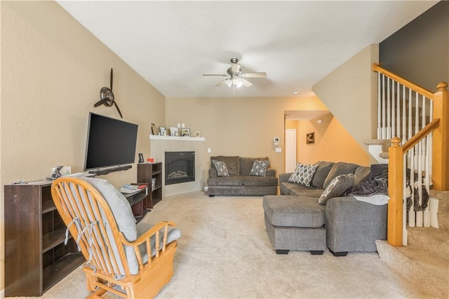 living area with carpet flooring, a ceiling fan, stairs, and a tile fireplace