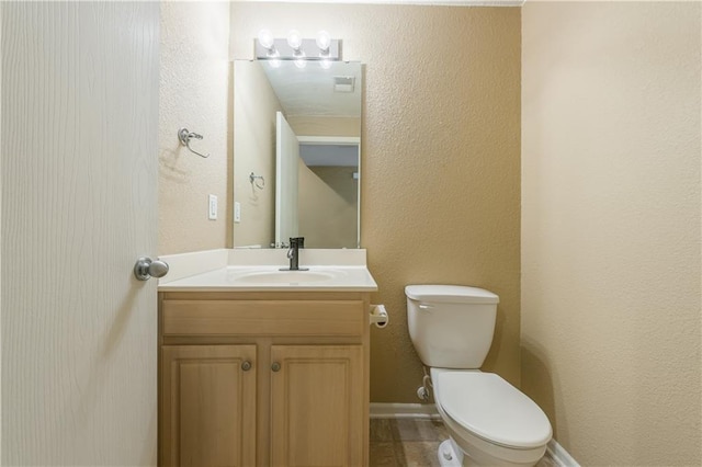 bathroom featuring vanity, toilet, a textured wall, and baseboards